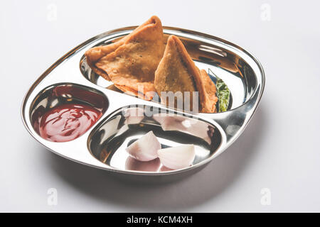Samosa - Indian deep fried junk but tasty food or snacks served in stainless steel plate over white background with tomato ketchup and green fried chi Stock Photo