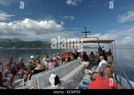 holiday makers or tourists on a boat trip in corfu, Greece on a bright sunny and partly cloudy day near the mountains. Stock Photo