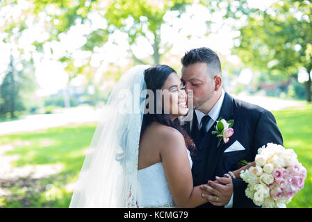 Groom kisses newlywed wife on her cheek in beautiful garden Stock Photo