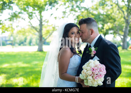 Bride and groom kissing in the park, Groom kissing bride on her cheek Stock Photo