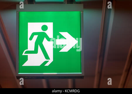 The emergency exit sign shows the direction of escape in case of danger. The emergency exit board hangs on the ceiling of the building. Stock Photo
