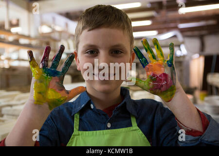 Boy showing colorful paint on his hands at pottery shop Stock Photo
