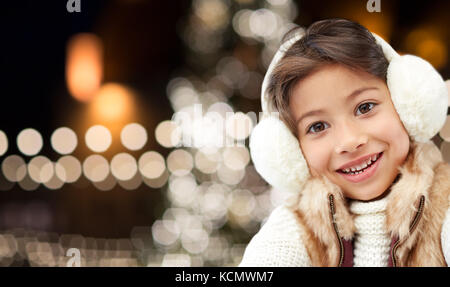 happy girl wearing earmuffs over christmas lights Stock Photo