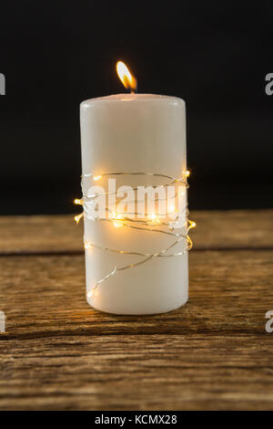 Close up of illuminated string lights wrapped on lit candle at table against black background Stock Photo