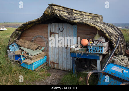 A disused boat now serving as a shed for a local fisherman sits upside down on the beach on Holy Island, on 27th September 2017, on Lindisfarne Island, Northumberland, England. Local fishermen on Holy Island considered it a sin to send boats to the junkyard. They instead found a way to transform their old herring boats into perfect little storage sheds for their nets, tools, and other equipment. The Holy Island of Lindisfarne, also known simply as Holy Island, is an island off the northeast coast of England. Holy Island has a recorded history from the 6th century AD; it was an important centre Stock Photo