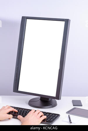 White blank pc monitor turned vertical and hand on keyboard on desk. Stock Photo