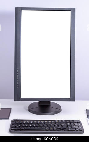 White blank pc monitor turned vertical and keyboard on desk. Stock Photo
