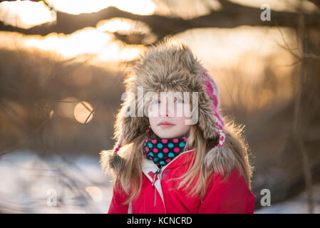 Girl (10) sitting in a tree on the shore of a frozen lake in winter. Stock Photo