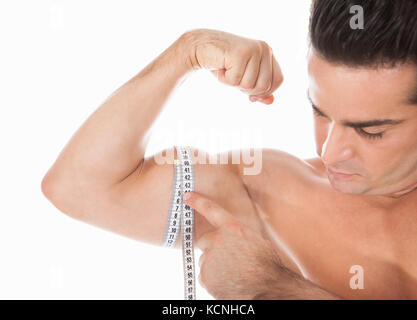 Impressive bicep on display. Muscular man measuring his bicep with a measuring  tape. Stock Photo by YuriArcursPeopleimages