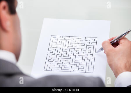 Close-up Of A Businessman Looking At Maze Puzzle Holding Pen Stock Photo