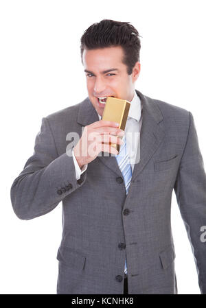 Portrait Of Young Businessman Biting Gold Bar Over White Background Stock Photo