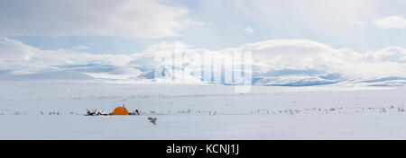 Snowmobilers camp under the McKenzie Mountains overlooking a high tundra plateau in the middle of winter's grip near Dechenla Lodge along the Canol Heritage Trail,  North west Territories, Canada Stock Photo
