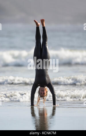 A female surfer shows off her gymnastic skills while playing on Chesterman Beach.  Tofino, Vancouver Island, British Columbia, Canada. Stock Photo