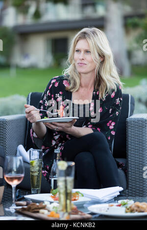 An attractive woman relaxes at an outdoor patio with food and drink while visiting the Kingfisher resort in Courtenay. Vancouver Island, British Columbia, Canada. Stock Photo