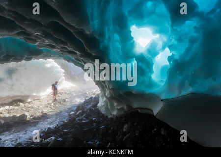 A hiker walks through a snow cave at the base of Century Sam lake, Strathcona Park, Vancouver Island, British Columbia, Canada. Stock Photo