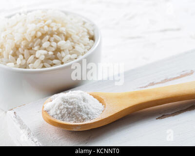 rice flour in wooden spoon and rice grains on white background. Copy space. Stock Photo