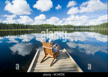 man sitting in chair on dock using a tablet, Two Mile Lake , Duck Mountain Provincial Park, Manitoba, Canada Stock Photo