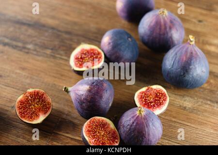 Ripe blue and purple figs, both whole and cut in half, randomly spilled on dark wood table Stock Photo