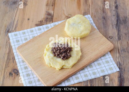 Potato dumplings stuffed with minced meat on a wooden cutting board. Step by step cooking. Healthy eating concept Stock Photo