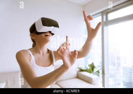 Young excited woman wearing VR headset touching objects in virtual world, using goggles mobile application for innovative education, shopping in 3d st Stock Photo