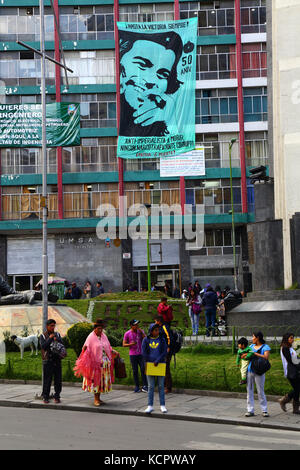 La Paz, Bolivia. 6th Oct, 2017. A banner to commemorate the 50th anniversary of Che Guevara's death hangs on the UMSA University Engineering Faculty building in La Paz city centre. Che was killed by Bolivian troops in La Higuera on 9th OCtober 1967; the government and social movements will be holding various events on that date at the location. In the foreground an Aymara woman wearing traditional dress is standing on the pavement Credit: James Brunker / Alamy Live News Stock Photo