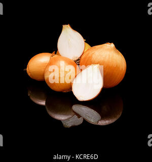 Pile of whole and cut onions with golden skin. On a black glossy background with real reflection. Stock Photo