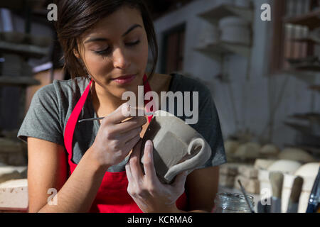 Female potter carving mug in pottery workshop Stock Photo