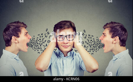 Two angry men screaming at peaceful guy covering his ears with hands ignoring them, alphabet letters coming out of mouth. Stock Photo