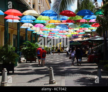 Port Louis, Mauritius - tourists and shoppers walk in an umbrella covered lane in the Le Caudan Waterfront in the capital Stock Photo