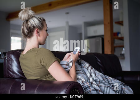 Woman using mobile phone while relaxing on sofa at home Stock Photo