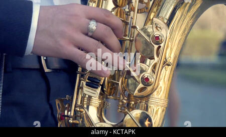 Hands of groom play on saxophone. Closeup hands of man playing golden alto saxophone with light effect. Men playing saxophone. Close up of men playing saxophone. golden alto in hands of young man. Stock Photo