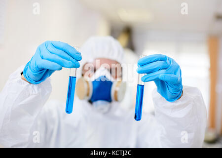 Close-up shot of unrecognizable chemist in protective clothing looking at test tubes with biohazard substance while working at modern laboratory Stock Photo