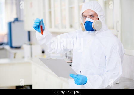 Waist-up portrait of confident virology research scientist posing for photography with test tube in hand while developing vaccine and taking notes on  Stock Photo