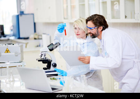 Cheerful group of microbiologists wearing safety goggles looking at test tube proudly while working together on creation of brand new cancer vaccine,  Stock Photo