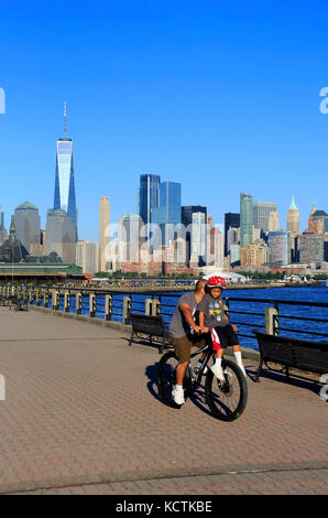 A man carrying a young boy on his bicycle in Liberty State Park with skyline of Lower Manhattan in background.Jersey City,New Jersey,USA Stock Photo