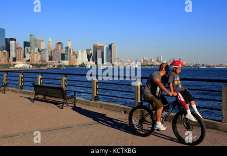 A man carrying a young boy on his bicycle in Liberty State Park with skyline of Lower Manhattan in background.Jersey City,New Jersey,USA Stock Photo