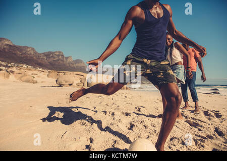 Group of friends playing football on the beach. Young people playing a soccer game on the seashore during summer vacation. Stock Photo