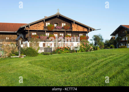 Farm houses with timber facade in traditional Bavarian style in Upper Bavaria with blooming flowers in the morning sun, Irschenberg, Bavaria, Germany Stock Photo