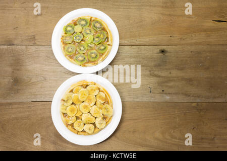 Waffle with milk caramel spread and kiwi fruit slices, another waffle with milk caramel spread and banana, on white plates, flat lay Stock Photo