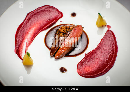 A gourmet dish of two slices of dark glazed meat cooked pink and topped with crumbs lies on a pool of dark sauce, framed by two arcs of bright red purée (possibly beetroot), on a white plate in the Hotel and Restaurant Kronenschlösschen in Hattenheim, Eltville am Rhein, Hesse, Germany. Two pale yellow cubes with small herb leaves and two dots of dark sauce complete the plate. The dish is part of the gala dinner cooked by Michelin-starred chef Thomas Kellermann on the evening of 8 March 2017 at the Kronenschlösschen. The dinner is part of the 21st Rheingau Gourmet & Wein Festival. It comprises  Stock Photo