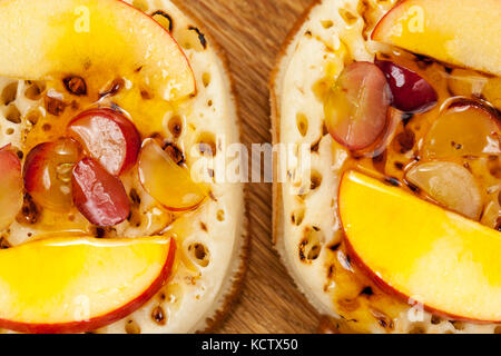 Close up shot of crumpets topped with apple segments, sliced grape and maple syrup Stock Photo