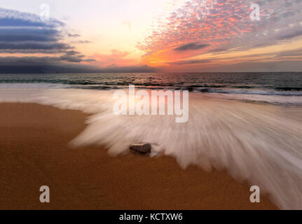 Sunset ocean is a serene scenic seascape on the beach with the bright sun setting on the ocean horizon as water rushes to the shore. Stock Photo
