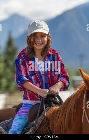 Attractive, young girl, sitting in the saddle, on a trail ride adventure. Looking at camera. Cranbrook, BC, Canada Stock Photo