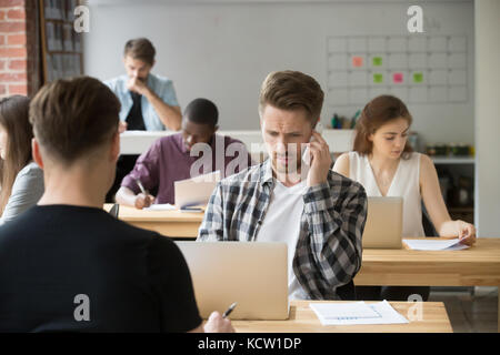 Perplexed casual entrepreneur making phone call at work in shared office space. Concerned project manager having unpleasant conversation with clients Stock Photo