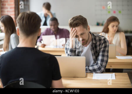 Perplexed, puzzled casual entrepreneur looks at laptop screen at workplace in shared office. Young project manager made serious mistake, lost document Stock Photo