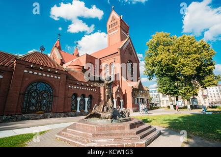 Minsk, Belarus. Sculpture Of Archangel Michael, Striking Dragon Snake Next To Main Facade Of Roman Catholic Church Of Saints Simon And Helena Or Red C Stock Photo