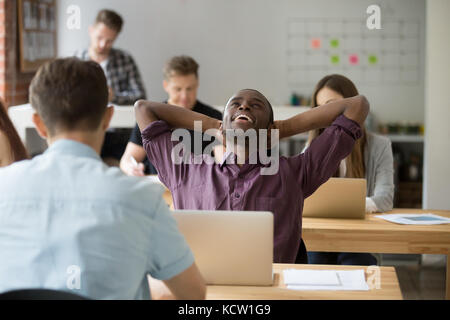 Relieved african american entrepreneur relaxing with hands behind head, happily resting after finished work. Office worker done with task before his c Stock Photo