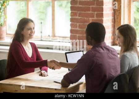 Smiling woman shaking hands with african american HR representative or new coworker. Employees greet each other before meeting, briefing about to star Stock Photo