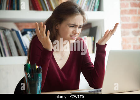 Perplexed female office worker shrugging while looking at laptop screen. Frustrated freelance businesswoman frustrated with confusing email from clien Stock Photo