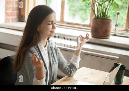 Calm businesswoman meditating in yoga pose in modern office setting. Business lady taking care of her health during break. Reducing discomfort at work Stock Photo